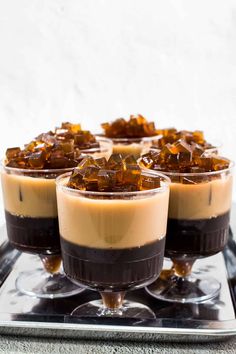 three glasses filled with chocolate pudding and caramel garnishes on a metal tray