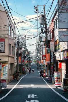 an empty street with lots of power lines above it and people walking on the sidewalk