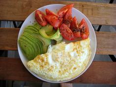 an omelet with tomatoes, avocado and tomato slices on a white plate