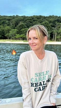 a woman is sitting on the edge of a boat and smiling at the camera with trees in the background