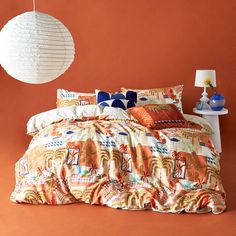 a bedroom with an orange wall and colorful bedding on the floor, along with a white hanging lamp