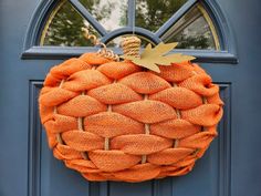 an orange burlock hanging on a blue front door with a gold leaf decoration