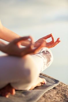 a person sitting on top of a rock with their hands in the air while doing yoga