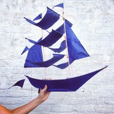 a hand holding up a blue sailboat made out of paper on a white brick wall