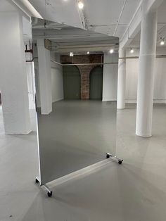 an empty room with white walls and flooring is shown in this image, there is a large mirror on the wall