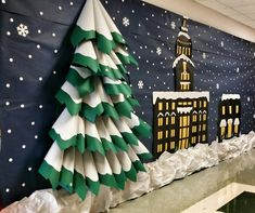 a decorated christmas tree in front of a wall with paper snow and buildings on it