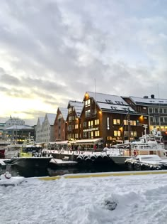 the boats are docked in the snow by the buildings on the water's edge