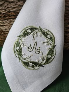 the monogrammed handkerchief is embroidered with flowers and leaves on white linen, along with a wicker basket