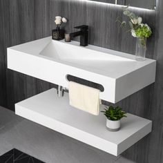 a white sink sitting under a bathroom mirror next to a plant and toilet paper dispenser