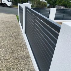 a black and white fence is next to a sidewalk with a truck in the background