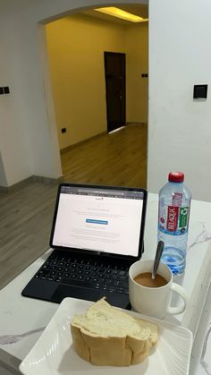 a laptop computer sitting on top of a table next to a cup of coffee and sandwich