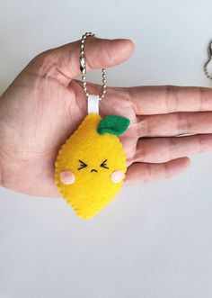 a hand holding a yellow keychain with a green leaf on it's head