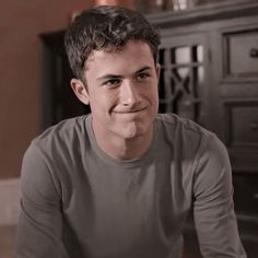 a young man sitting on the floor in front of a dresser smiling at the camera