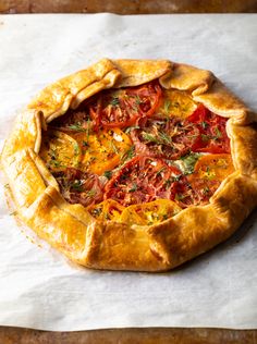 a freshly baked tomato pie on top of a piece of parchment paper with herbs sprinkled all over it