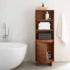 a white bath tub sitting next to a wooden shelf filled with folded towels and blankets