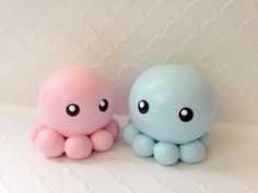 two small toys sitting next to each other on a white tableclothed surface, one is blue and the other is pink