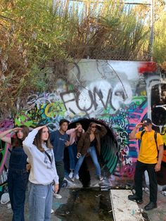 a group of people standing in front of a graffiti covered wall