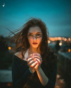 a woman is holding her hands together in front of the camera with lights behind her