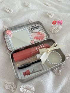 an open tin with various items in it on a white bed sheet and pink flowers