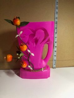 a pink vase sitting on top of a table next to a measuring tape and oranges