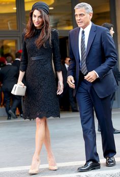 a woman in a black dress and a man in a suit walking down the street