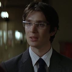 a young man wearing glasses and a suit in a dark room with light from the ceiling