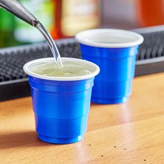 two plastic cups filled with green liquid on top of a wooden table