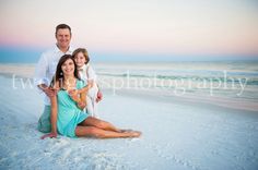 a family sitting on the beach in front of the ocean at sunset with their arms around each other