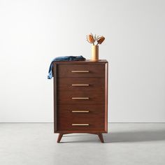 a wooden cabinet with three drawers and a blue blanket on the top, in front of a white wall