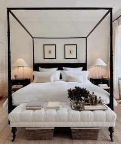 a bedroom with a four poster bed and white linens on the headboard, footstools, lamps and pictures above it