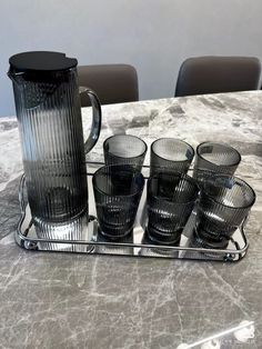 a glass pitcher and six glasses on a tray with marble table top in the background