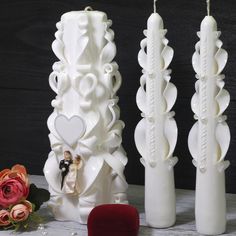 three tall white candles are next to each other with hearts on them and flowers in the foreground