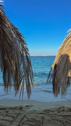 two straw umbrellas sitting on top of a sandy beach