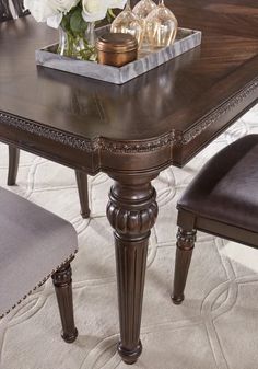 a dining room table with two chairs and a tray on it's end, in front of a white flower arrangement