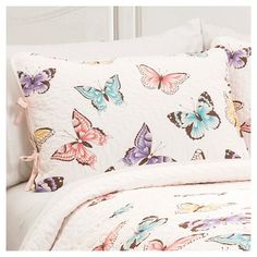 a white bed with butterflies on it and a pink pillow case next to the headboard