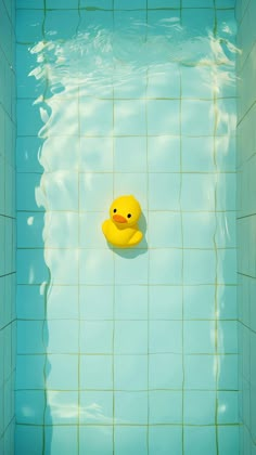 a yellow rubber duck floating in a blue swimming pool with green tiles on the walls