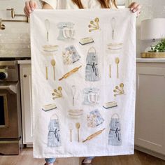 a woman holding up a tea towel with kitchen utensils on it