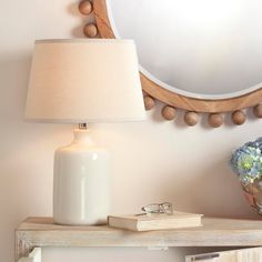 a table with a lamp, mirror and book on it next to a flower vase