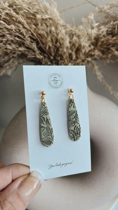 a pair of earrings is being held in front of a white vase with dried grass