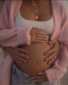 a pregnant woman is holding her stomach with both hands and wearing gold rings on it