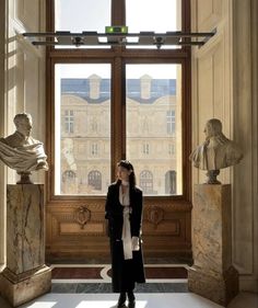 a woman standing in front of a large window next to busturines and statues