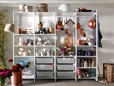 a white shelf filled with pots and pans on top of wooden floor next to plants