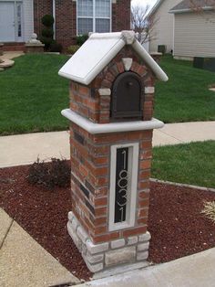 a brick mailbox in front of a house with a white roof and chimney cover