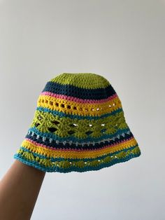 a crocheted hat is being held up to the sky by someone's hand