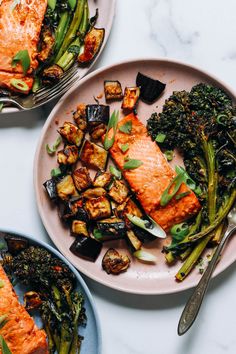 two plates with salmon, broccoli and other food items on top of them