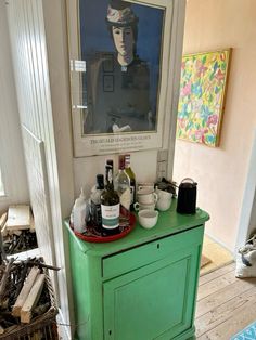 there is a green cabinet with bottles on it in front of a painting and other items