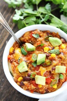 a white bowl filled with chili and avocado on top of a wooden table