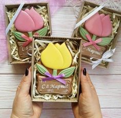 three decorated cookies in a box with ribbon tied around the edges, and one being held by a woman's hand