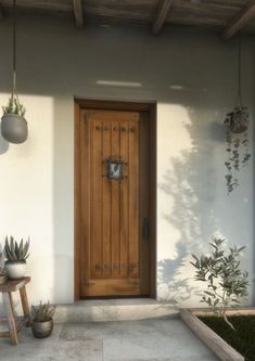 a wooden door sitting on the side of a white wall next to potted plants