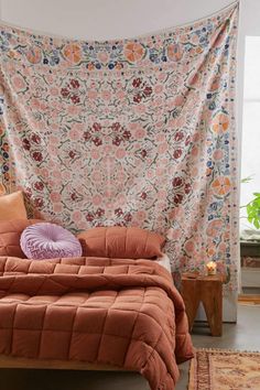 a bed with an orange comforter in front of a floral tapestry hanging on the wall